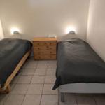 Two single beds with gray bedding and wooden dresser in a room with tiled floor.