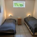 Two beds with gray covers, a small cabinet, and a window with a view of greenery.