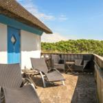 Terrasse mit Liegestühlen, Tisch und Grill vor einem Haus mit Strohdach und blauer Tür.