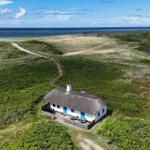 Wohnhaus mit Strohdach und blauen Türen auf grüner Dünenlandschaft mit Blick auf das Meer.