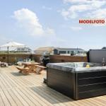 Terrasse mit Whirlpool, Grill und Holztisch unter einem Sonnenschirm.