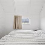 Bedroom with white wood paneling, bed, and small window with curtain.