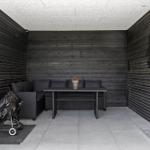 Outdoor area with seating, table, and grill. Black wooden walls and concrete floor.