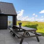 Terrace with wooden table and benches in front of a house with roof and glass facade.