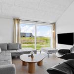 Living room with sofa, chairs, and TV. Large windows show landscape.