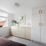 Schlafzimmer mit Fenster, Schrank und Schreibtisch. Draußen ist ein Garten mit Haus.