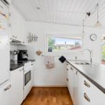 Küche mit weißen Schränken, dunkler Arbeitsplatte und Holzboden. Fenster und Tür zu Außenbereich.