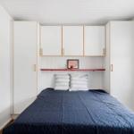 Schlafzimmer mit Bett, weißen Schränken und rotem Regal.