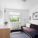 Ein Raum mit weiß verkleideten Wänden, einem Fenster und einem Sofa mit Kissen.