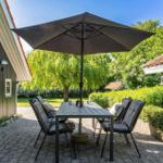 Terrace with table, chairs, and umbrella between houses and greenery.