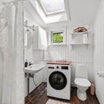 Bathroom with shower, washing machine, and toilet. Window and skylight provide daylight.