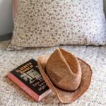 A straw hat and a book rest on a patterned bedspread.