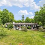 Black house with terrace and garden, surrounded by trees under blue sky.