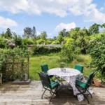 Deck with table, chairs, and bench. Green garden and sky in the background.