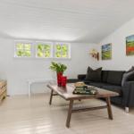 Living room with gray sofa, wooden table, and windows. Wall art and plants.