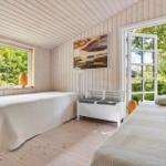 Two beds in a room with wooden walls and windows overlooking greenery.
