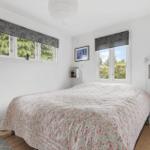 Bedroom with bed, two windows, and wooden floor.