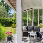 Patio with seating, glass walls, and garden view. White tables and plants.