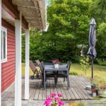 Deck with table, chairs, and umbrella beside red house with green garden.