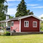 Red wooden house with terrace, garden, and grill area under blue sky.