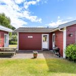 Red wooden house with patio, grill, and seating area in the garden.