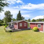 Red wooden house with terrace and garden under blue sky.