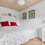 Bedroom with bed, white walls and wooden floor. Pictures and a mirror hang on the wall.