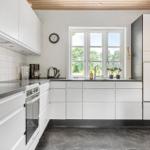 Moderne Küche mit weißen Schränken, dunklem Arbeitsplatz und Fenster mit Blick auf Grün.