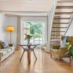 Wohnzimmer mit Sofa, Sessel, Tisch und Treppe. Fenster zur Außenseite.