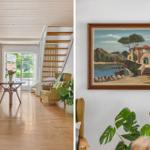 Wohnraum mit Holzboden, Sofa, Sessel und Treppe. Wandbild zeigt Küstenlandschaft.