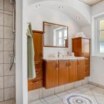 Badezimmer mit Holzschrank, Dusche und Fenster mit Kerzen.