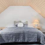 Schlafzimmer mit Dachschrägen, Bett mit grauer Bettwäsche und Nachttisch mit Lampe.