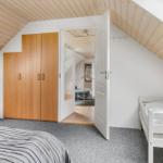 Schlafzimmer mit Dachschräge, Kleiderschrank und Bett. Tür führt in Wohnbereich.