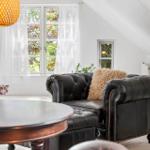 Wohnzimmer mit schwarzem Ledersofa, runden Tisch und Fenster mit Blick auf Grün.