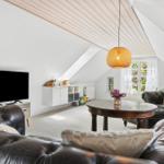 Wohnraum mit schwarzem Ledersofa, runden Tisch und TV an der Wand.