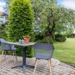 Garten mit Tisch und zwei Stühlen, umgeben von Bäumen und Sträuchern.