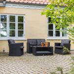 Terrasse mit Sitzgruppe, Pflanzen und gelbem Haus mit Fenstern.