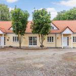 Ein gelbes Haus mit rotem Dach und mehreren Eingängen, umgeben von Bäumen und Kies.