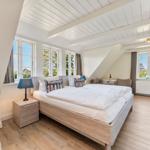 Schlafzimmer mit Doppelbett, Fenstern und Holzboden.