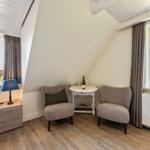 Zimmer mit zwei Sesseln, Tisch, Bett und Fenstern mit Blick.
