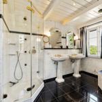 Badezimmer mit Dusche, zwei Waschbecken und Badewanne, weiße Marmorwände und schwarze Fliesen.