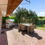 Terrasse mit Esstisch, Stühlen und Strandkorb. Hinterhof mit Rasen und Bäumen.