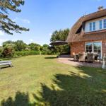 Haus mit strohgedecktem Dach, Garten mit Liegestühlen und Terrasse mit Tisch und Stühlen.