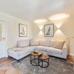 Wohnzimmer mit Ecksofa, zwei Tischen und Wandbildern. Tür und Schrank sind sichtbar.