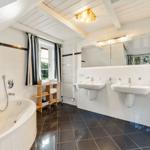 Bad mit Badewanne, zwei Waschbecken und Fenster mit Vorhängen.