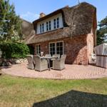 Haus mit Strohdach, Terrasse mit Tisch und Stühlen, Strandkorb und Grünflächen.