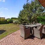 Terrasse mit Esstisch und Stühlen, umgeben von Grün und einem großen Baum.