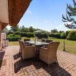 Terrasse mit Esstisch und Stühlen, Blick auf grünen Garten mit Hecken und Baum.