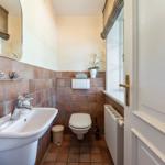 Badezimmer mit Waschbecken, Toilette und Fenster. Wand- und Bodenfliesen in Terrakottaton.