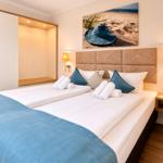Zimmer mit Sofa, Fenster, Wandbild und Regal mit Dekorationsgegenständen.